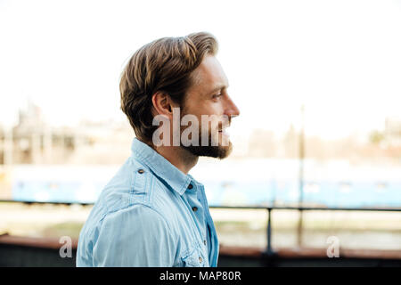 Profil de l'homme blond beau décontracté à l'extérieur en chemise bleue, souriant et avoir une attitude positive Banque D'Images