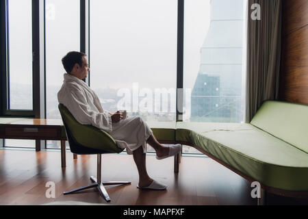 L'homme en peignoir de boire du café, à la recherche à Cityscape Banque D'Images