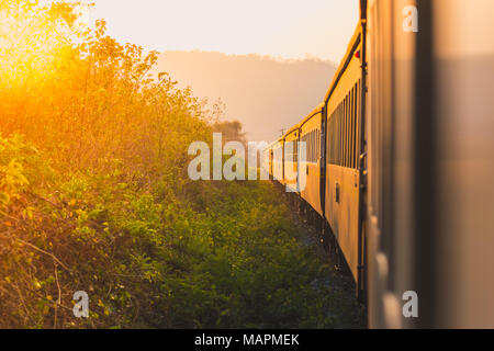 Au coucher du soleil voyage en train. Vue d'un train à partir de la fenêtre d'un train, le soleil couchant dans la gauche parmi la végétation et une lointaine colline rose. Banque D'Images