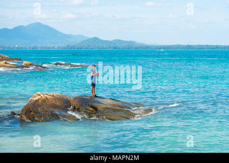 Un homme poissons avec une roue tournante debout sur un rocher situé dans la sarcelle d'eau de mer du golfe de Thaïlande. Banque D'Images