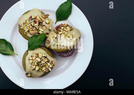 Le basilic vert muffins au chocolat blanc fondu sur la plaque blanche sur fond noir. Les feuilles de basilic et la pistache topping. Bonbons sains Banque D'Images