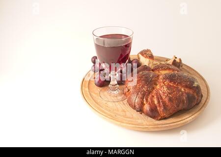 Un plateau en bois avec du pain fait maison, un verre de vin rouge et quelques raisins rouges sur un fond blanc. Banque D'Images