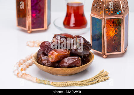 Ramadan Kareem festif, Close up de dates sur plaque de bois et chapelet avec lampes lanternes orientales et tasse de thé noir sur fond blanc. Jours fériés islamiques Banque D'Images