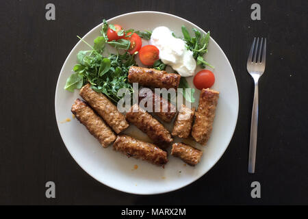 Ćevapi serbe également connu comme ćevapčići servi avec des tomates cerises et les lance dans la plaque sur la table. Banque D'Images