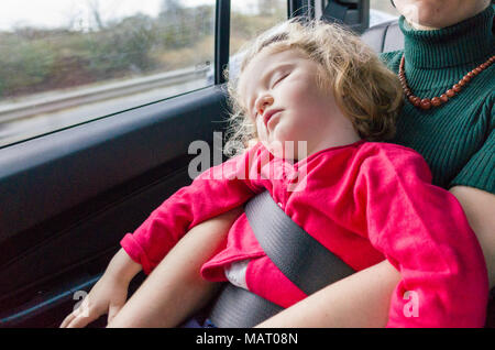 Chambre enfant de deux ans équitation de siège arrière de voiture sur les genoux de la mère à l'aide de la ceinture de sécurité, l'UK Banque D'Images