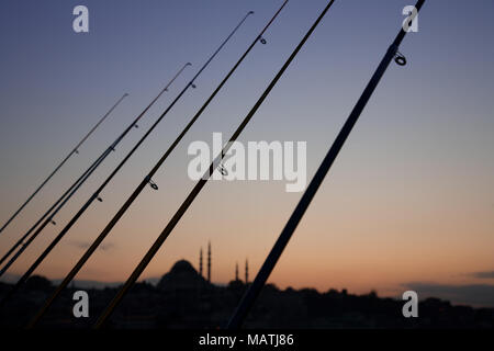 Une rangée de cannes à pêche et la mosquée lointaine silhouette au coucher du soleil depuis le pont de Galata à Istanbul, Turquie. Banque D'Images
