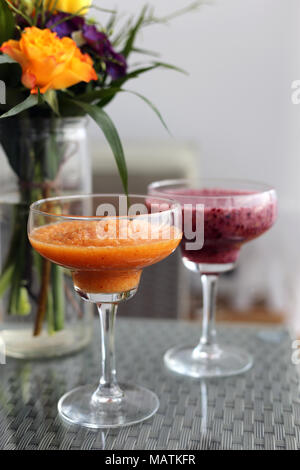 Bricolage maison deux smoothies (berry Smoothie orange et violet) sur un balcon table avec des fleurs colorées en arrière-plan. Sain et Délicieux ! Banque D'Images