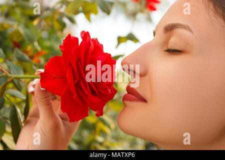 Jeune belle Caucasian girl smelling roses rouges dans le jardin aux beaux jours. Banque D'Images