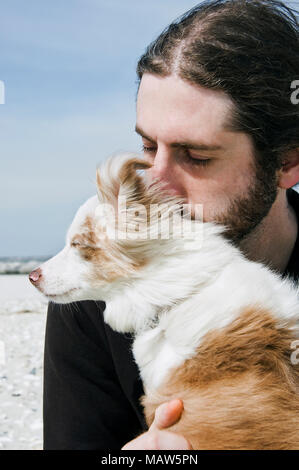 Un homme assis sur la plage avec son chien. Banque D'Images