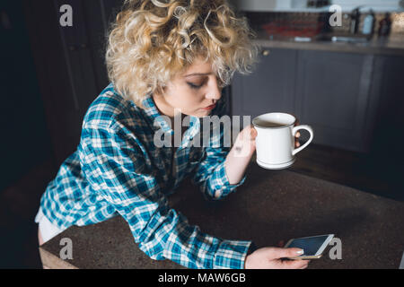 Woman having coffee lors de l'utilisation de téléphone mobile dans la cuisine Banque D'Images