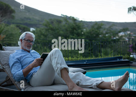 Senior man reading a book proche piscine Banque D'Images