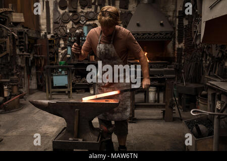 Blacksmith hammering une tige de métal chaud Banque D'Images