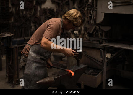 Blacksmith hammering une tige de métal chaud Banque D'Images