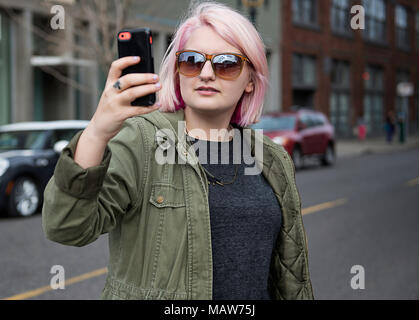 Une jeune femme aux cheveux roses, debout dans la rue, à Portland en utilisant son téléphone portable pour prendre une photo. Banque D'Images