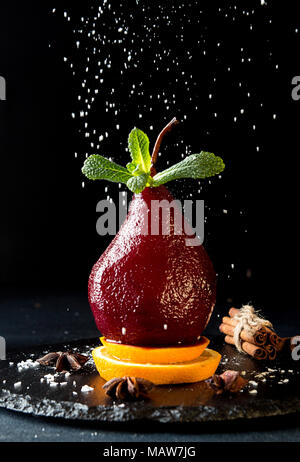 Les Poires au vin. Compote de poires dessert traditionnel au vin rouge sur fond noir. Poudre de Sucre strewing ci-dessus. Banque D'Images