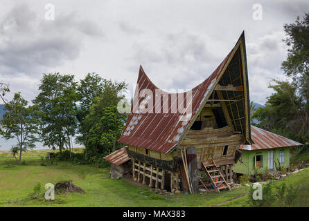 Une vieille maison de style traditionnel de l'architecture Batak avec châssis en bois et des sculptures se trouve sur la banque sur l'immense lac de cratère Lac Toba, Sumatra, Indonésie Banque D'Images