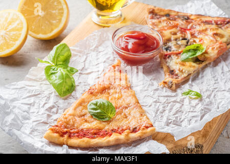 Deux morceaux de pizza aux champignons et fromage et aussi avec les tranches de citron et les feuilles de basilic sur une planche en bois recouverte de papier cuisson, servi avec Tom Banque D'Images