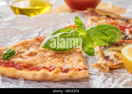 Deux morceaux de pizza aux champignons et fromage et aussi avec les tranches de citron et les feuilles de basilic sur une planche en bois recouverte de papier cuisson, servi avec Tom Banque D'Images