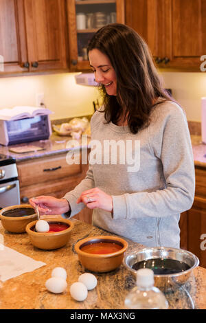 Femme à la teinture des oeufs de Pâques dans la cuisine Banque D'Images