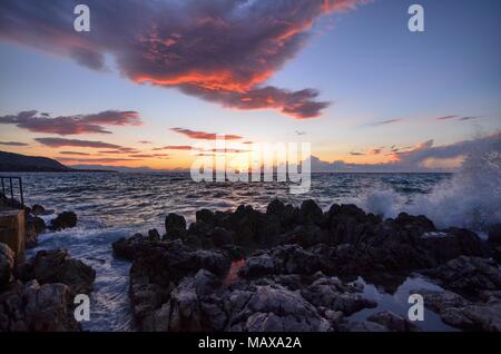 Cefalù, Italie, Sicile le 16 août 2015. Le coucher de soleil vu depuis le port de Cefalù. Ciel en feu et lave-réflexions colorées au milieu des rochers . Banque D'Images