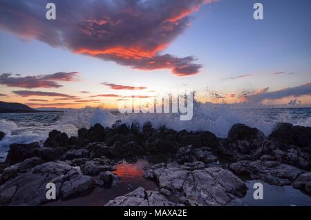 Cefalù, Italie, Sicile le 16 août 2015. Le coucher de soleil vu depuis le port de Cefalù. Ciel en feu et lave-réflexions colorées au milieu des rochers . Banque D'Images