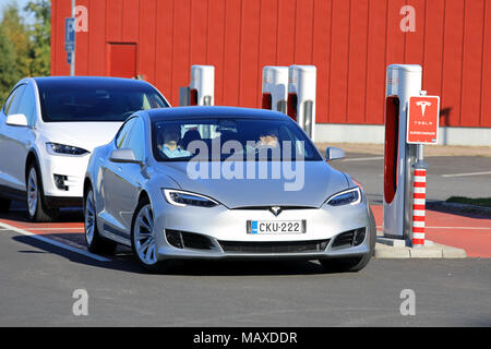 TOIJALA, FINLANDE - le 24 septembre 2017 : Deux jeunes hommes en argent Tesla Model S lifting laisser voiture électrique Supercharger, avec blanc Modèle Tesla Banque D'Images