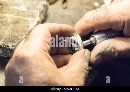 Polissage d'un bijoutier homme bague argent avec l'aide d'un mandrin pour papier de verre, montés sur un arbre flexible. Banque D'Images