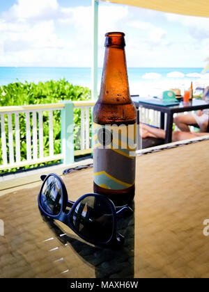 Bouteille de bière à côté de lunettes sur la table, avec une superbe vue sur la plage aux eaux turquoises à Grace Bay, Providenciales, Îles Turques et Caïques. Toile Banque D'Images