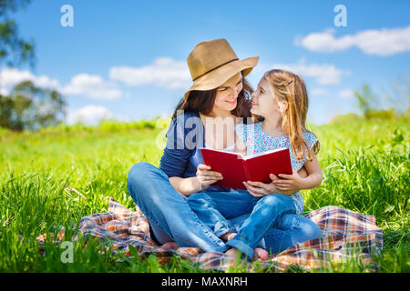 Mère et fille aime lire livre assis sur pré vert dans le parc d'été Banque D'Images