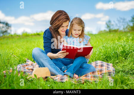 Mère et fille aime lire livre assis sur pré vert dans le parc d'été Banque D'Images