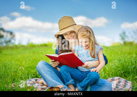 Mère et fille aime lire livre assis sur pré vert dans le parc d'été Banque D'Images