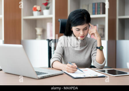 Portrait d'une belle asiatique young businesswoman sitting dans le bureau, tenant le document et de penser. Banque D'Images