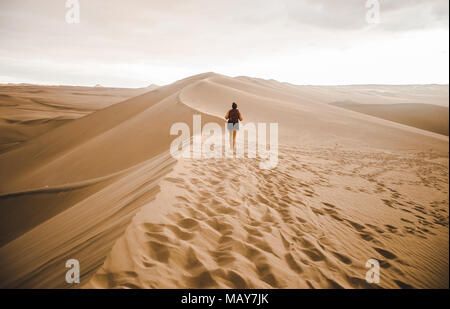 Jeune femme millénaire / promenades touristiques voyageur sur une dune de sable dans le désert avec un sac à dos rouge, le Pérou Huacachina dans Banque D'Images