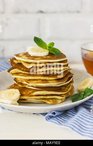 Des crêpes de bananes en plaque blanche et une tasse de thé sur le linge bleu sur fond blanc Banque D'Images