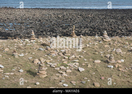 cairns en pierre empilés sur la plage rocheuse de Holy Island, Northumberland, Angleterre sous la lumière douce de la côte, symbolisant la paix et la réflexion. Banque D'Images