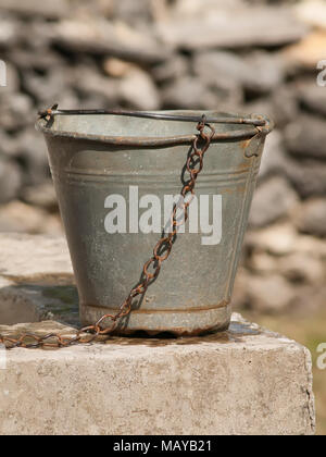 Poterie rétro. Vieux seau d'eau rouillée sur bien avec chaîne et fond de pierre bleuie. Banque D'Images