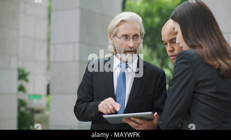 Les cadres d'entreprise multinationale discuter affaires using digital tablet. Banque D'Images