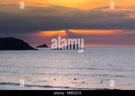 La Poule et le poussin de petites îles au large de pointe sont seeen Pentire en silhouette alors que le soleil se couche sur Cornwall dans Fistral. Banque D'Images