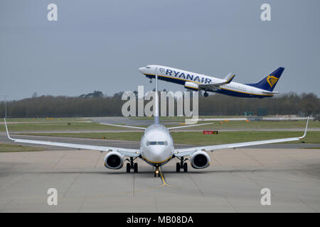 Le roulage des avions de Ryanair à l'aéroport de Londres Stansted Ryanair comme un autre avion décolle dans l'arrière-plan Banque D'Images