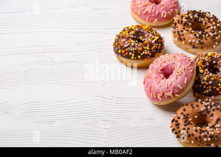 De délicieux beignets avec glaçage multicolore et mise sur fond de bois blanc. Copy space Banque D'Images