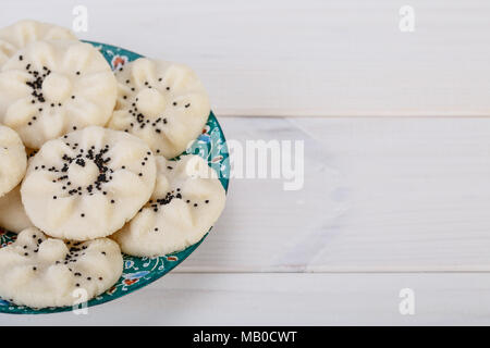 Close up image of Persian en forme de fleur de riz sucré Cookies (Naan Berenji) avec les graines de pavot dans un design traditionnel en bois blanc sur plaque turquoise bac Banque D'Images