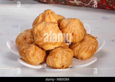 Frais Profiteroles profiteroles gâteaux remplis de crème pâtissière dans une assiette blanche sur fond de bois blanc dessert persan populaire. Banque D'Images