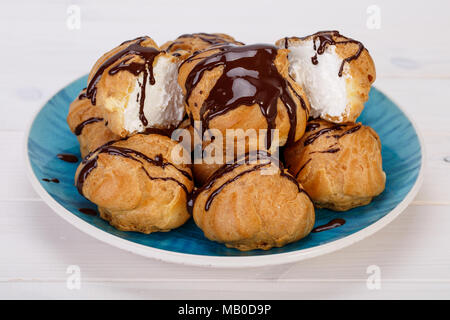 Frais Profiteroles profiteroles gâteaux remplis de crème pâtissière et garni de sauce au chocolat dans une plaque bleu turquoise sur fond blanc. populaires P Banque D'Images