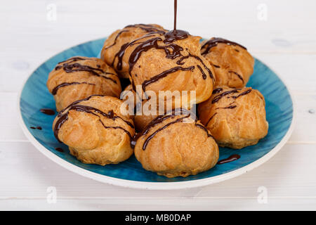 Frais Profiteroles profiteroles gâteaux remplis de crème pâtissière et garni de sauce au chocolat dans une plaque bleu turquoise sur fond blanc. populaires P Banque D'Images