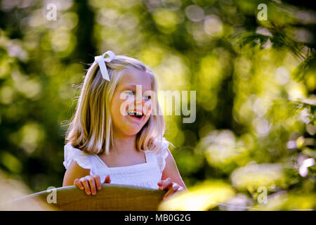 Un petit sourire rétroéclairé Caucasian girl en robe blanche avec fond vert floue Banque D'Images