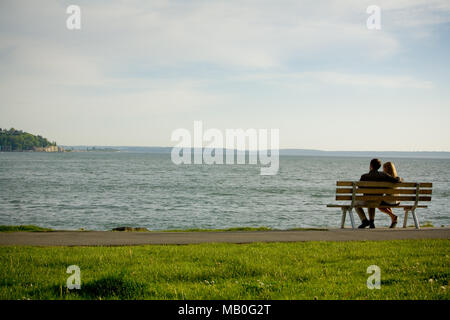 Un jeune couple assis à une chaise à l'extérieur, vers la mer à un parc au bord de l'eau dans le centre-ville de Seattle Banque D'Images