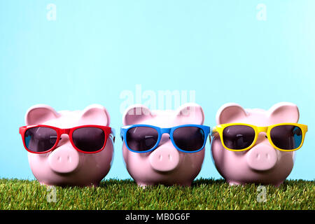 Trois tirelires rose avec des lunettes de soleil sur l'herbe avec ciel bleu. Studio shot avec un fond bleu. Banque D'Images