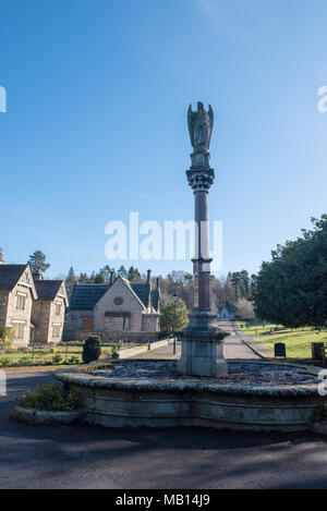 Colonne ornée d'un ange et fontaine en pierre dans un village britannique historique sous un ciel bleu clair par un matin lumineux Banque D'Images