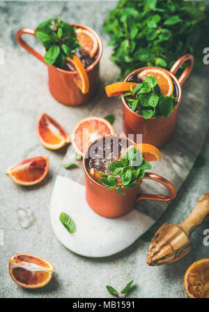 Moscou orange sanguine alcool mule de cocktails avec feuilles de menthe fraîche et de la glace dans des tasses de cuivre à bord sur fond de béton gris, selective focus Banque D'Images