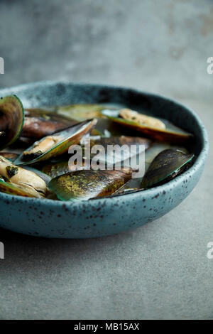 Les moules à Kiwi marinier sauce avec le vin blanc et le persil dans la main, plaque céramique bleu sur fond gris Banque D'Images